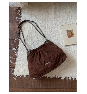 Detail of dark brown quilted suede bucket bag with silver metal chain and logo