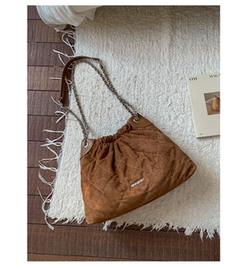 Detail of brown quilted bucket bag with chain strap and logo on white plush carpet