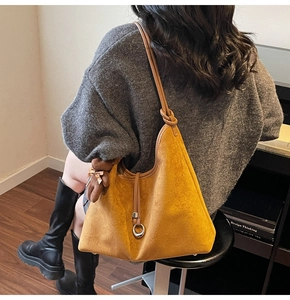 Detail of mustard yellow suede tote bag with metal ring and teddy bear charm accessory