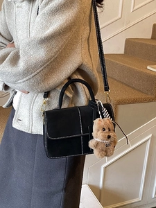 Chic black crossbody bag with white stitching and plush puppy charm on a female model