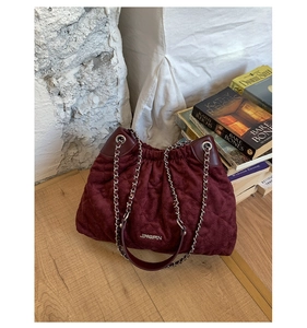 Detail of burgundy quilted suede bucket bag with silver chain and metal logo