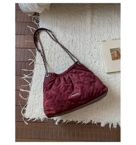 Close-up of quilted burgundy suede bucket bag with silver metal chain strap on soft rug