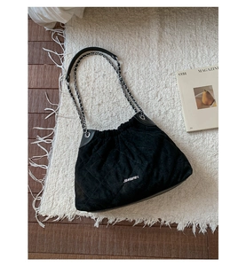 Close-up of black quilted suede bucket bag featuring chain strap and silver hardware