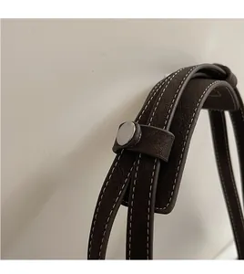 Détail de la poignée en cuir marron avec coutures blanches et rivets argentés