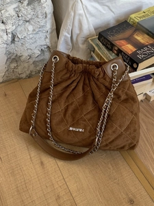 Brown quilted crossbody bucket bag with chain strap and drawstring closure on a wooden table