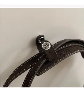 Détail de cuir grainé marron foncé avec coutures blanches et bouton pression argenté
