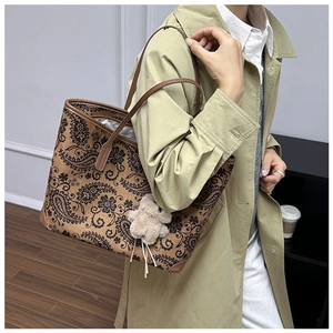 Detail of vintage printed tote bag with plush bear charm worn with a stylish trench coat