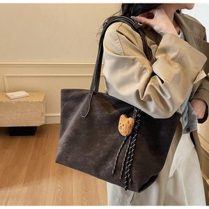 Détail du sac cabas en daim marron foncé avec surpiqûres blanches et breloque ours