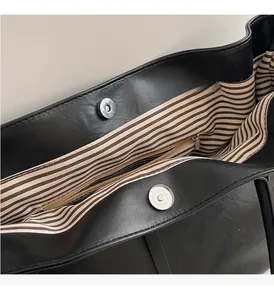 Detail view of large black tote bag featuring magnetic buckles and striped fabric lining