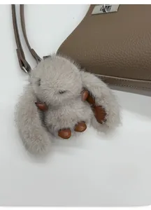 Gros plan sur un charm lapin en peluche grise avec détails en cuir sur un sac brun