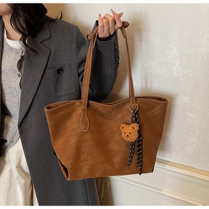 Détail d'un sac cabas marron mat avec breloque d'ours sur un mannequin en blazer