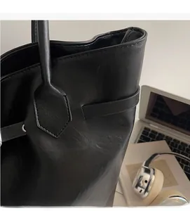 Detail of black pebbled leather tote bag with reinforced stitching on a workspace desk