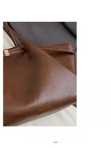 Détail de la texture cuir grainé marron et boucle dorée d'un grand sac cabas