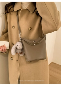Détail du sac seau taupe avec texture lychee, breloque lapin en peluche et fermoir métal