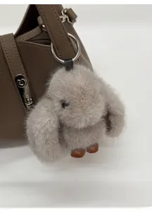 Close-up of a taupe plush rabbit charm with metal ring on a brown leather handbag
