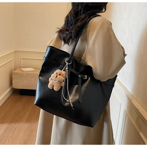 Detail of a large black faux leather tote bag with long straps and a plush bear charm