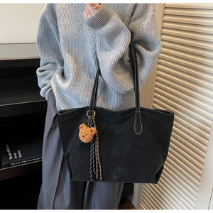 Détail du sac cabas en daim noir avec coutures blanches et charm d'ours peluche