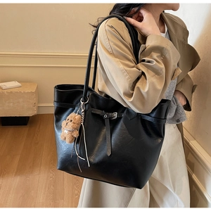 Detail of black faux leather tote bag featuring a cute brown plush bear charm and thin straps