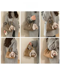 Detail of khaki leather bucket bag with metal lock and plush rabbit charm on a gray coat
