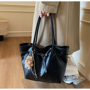 Detail of a large black tote bag with glossy leather finish and cute bear charm pendant