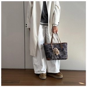 Close-up of vintage paisley tote bag featuring brown leather trim and a plush bear charm