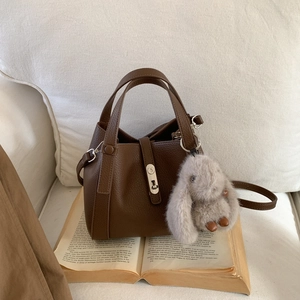 Detail of dark brown lychee pattern leather tote bag with silver lock and plush bunny charm