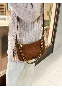 Detail of brown suede crescent bag with beaded charm and chain strap on shoulder