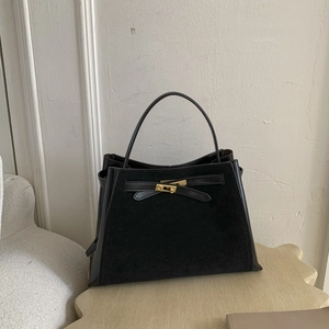 Close-up of black suede and leather handbag with gold metal twist lock and strap