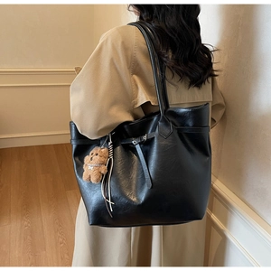 Close-up of a large black faux leather tote bag with a cute brown plush bear charm