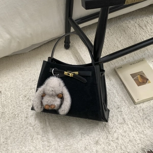 Detail shot of black faux suede bucket bag with gold buckle and plush rabbit charm on rug