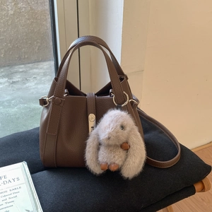 Detail of brown lychee leather bucket bag with silver buckle and plush rabbit charm