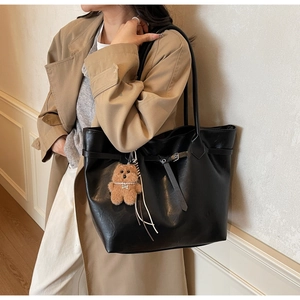 Detail of large black matte faux leather tote bag with brown plush bear accessory