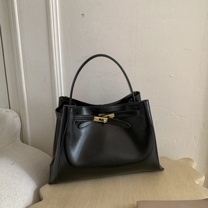 Detail of matte black leather bucket bag featuring gold buckle and retro belt design