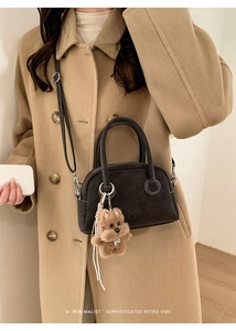Dettaglio borsa in pelle opaca marrone scuro con cuciture bianche e ciondolo peluche