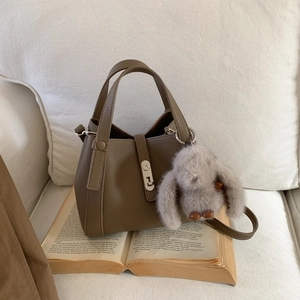 Close-up of brown litchi pattern bucket bag with silver buckle and plush rabbit charm