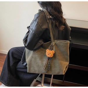 Détail du sac cabas en daim vert avec surpiqûres blanches et breloque ours orange
