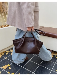 Détail d'un grand sac à main marron foncé avec boucle sur un banc d'automne avec feuilles