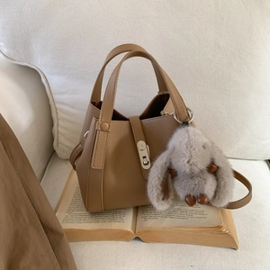 Detail of tan lychee grain bucket bag with metal buckle and plush bunny charm
