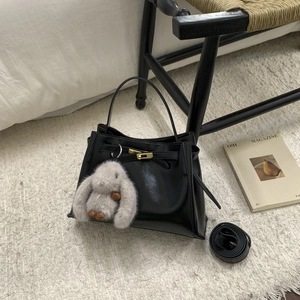 Detail of black leather bucket bag with gold hardware lock and grey plush bunny charm
