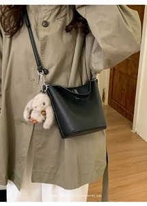 Gros plan du sac seau noir en cuir grainé avec breloque lapin blanc et bandoulière