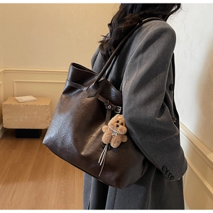 Detail of dark brown tote bag with side strap accents and cute plush bear charm