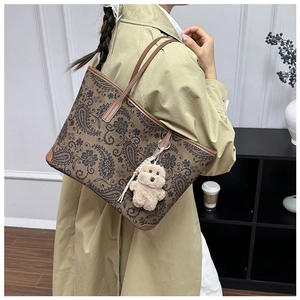 Detail of vintage paisley tote bag featuring brown leather straps and a plush bear charm