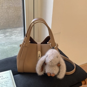 Close-up of brown litchi pattern leather handbag with metal lock and plush rabbit charm