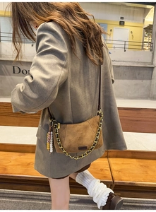 Close-up of brown suede crossbody bag with metal chain strap and colorful beaded charm