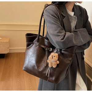 Detail of dark brown tote bag with leather texture and cute plush bear charm accessory