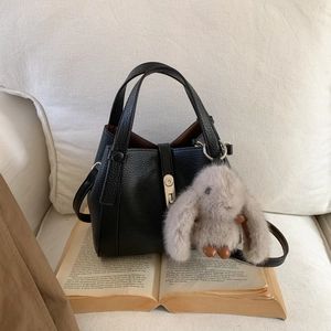 Close-up of black lychee grain leather handbag with silver lock and grey plush bunny charm