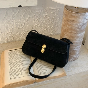 Close-up of a matte black suede shoulder bag with a gold metal clasp on an open book