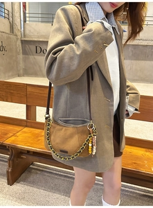 Detail of suede crescent shoulder bag with golden chain and colorful bead charm on a model
