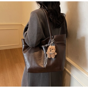 Deep brown tote bag with bear charm shown from side view on model for size perspective