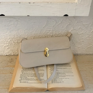 Macro shot of minimalist beige underarm bag featuring a metallic gold twist-lock closure